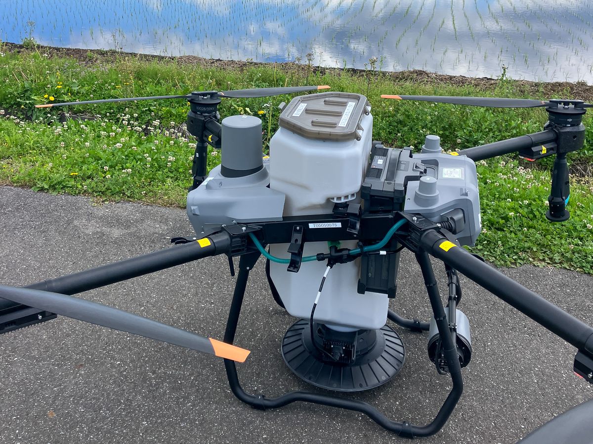 DJI Agras T25農業用ドローンの機体全体。奥に代かき後の水田